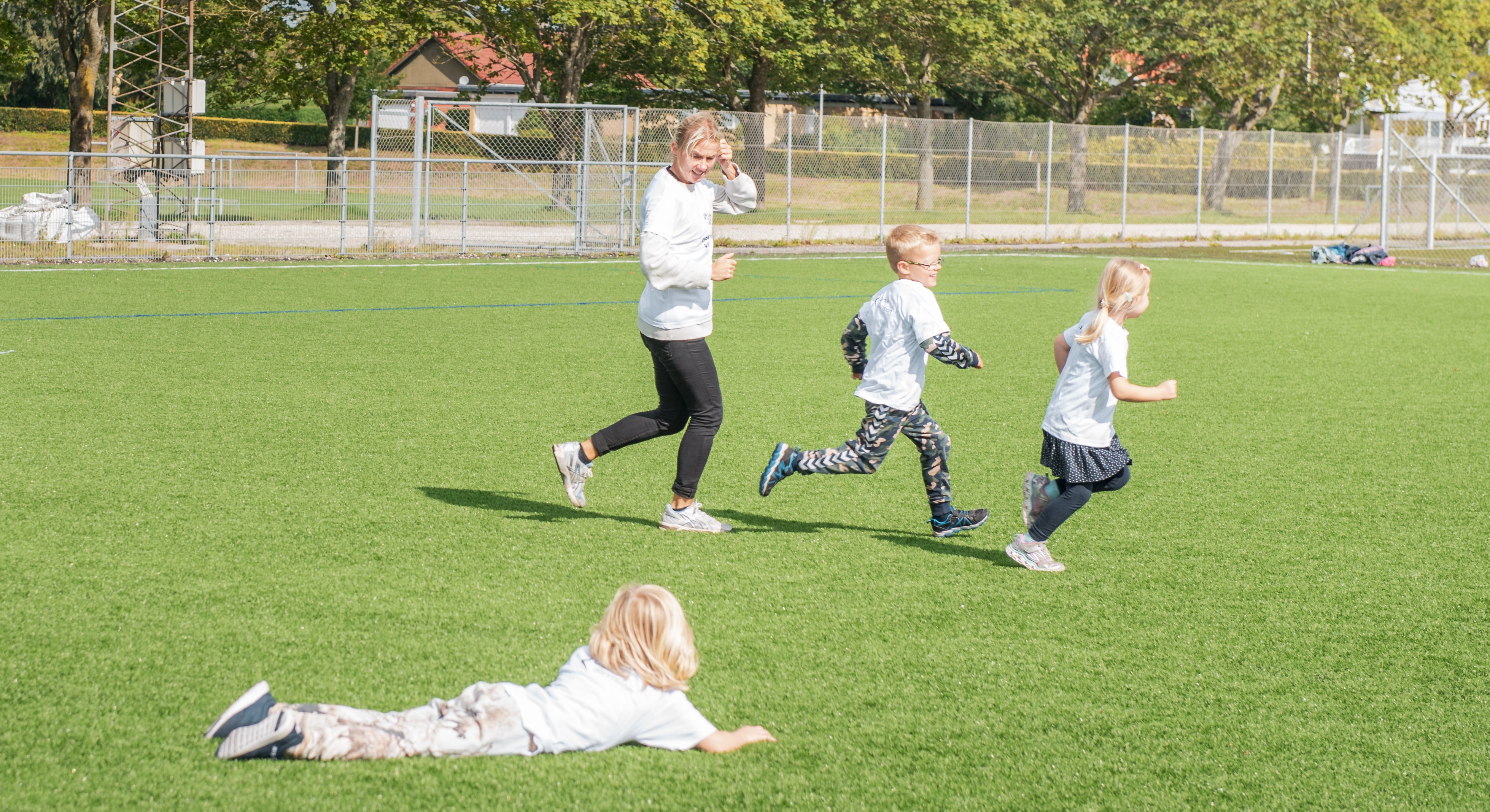 Børn og træner løber på fodboldbane