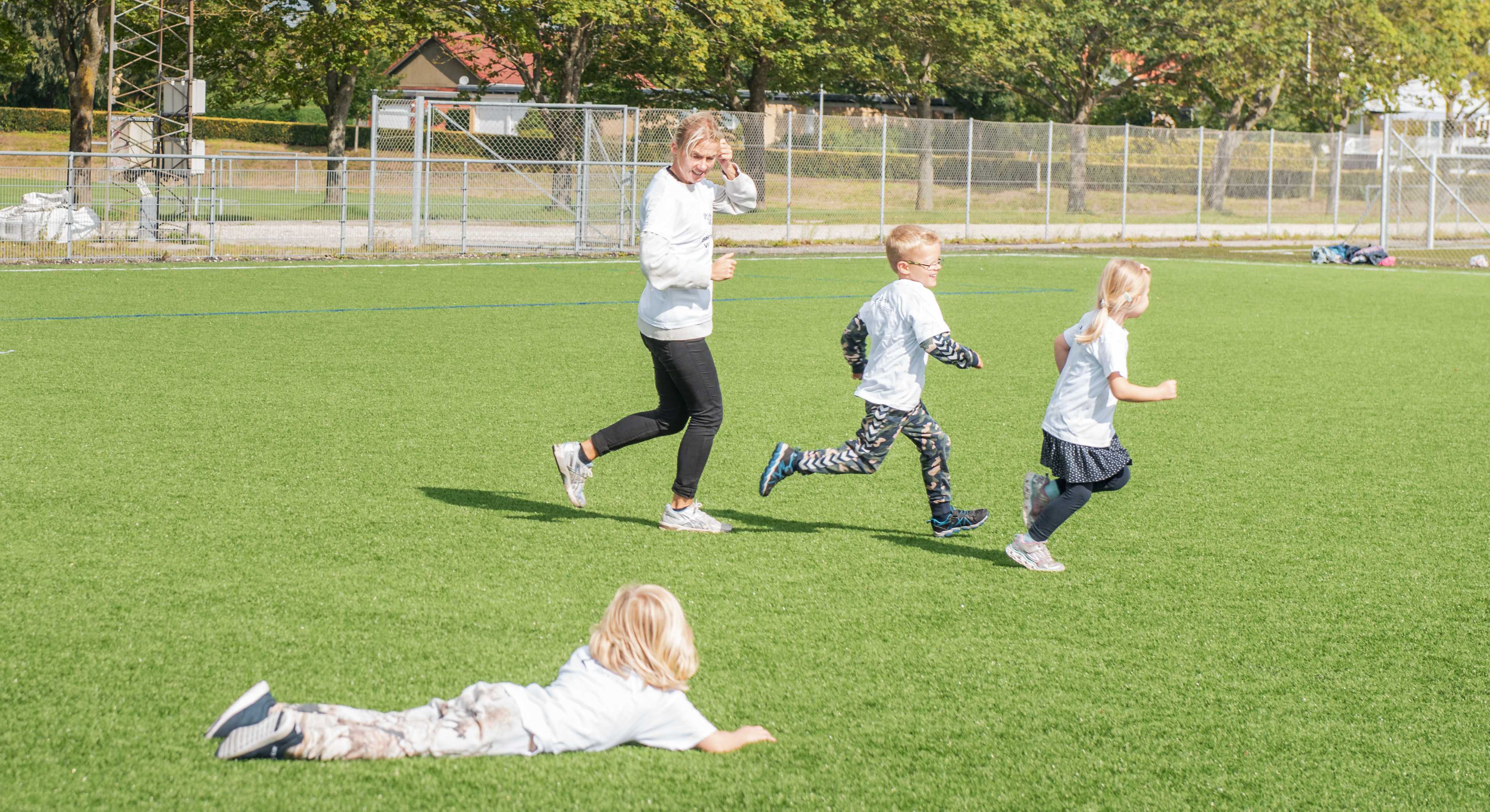 Børn og træner løber på fodboldbane
