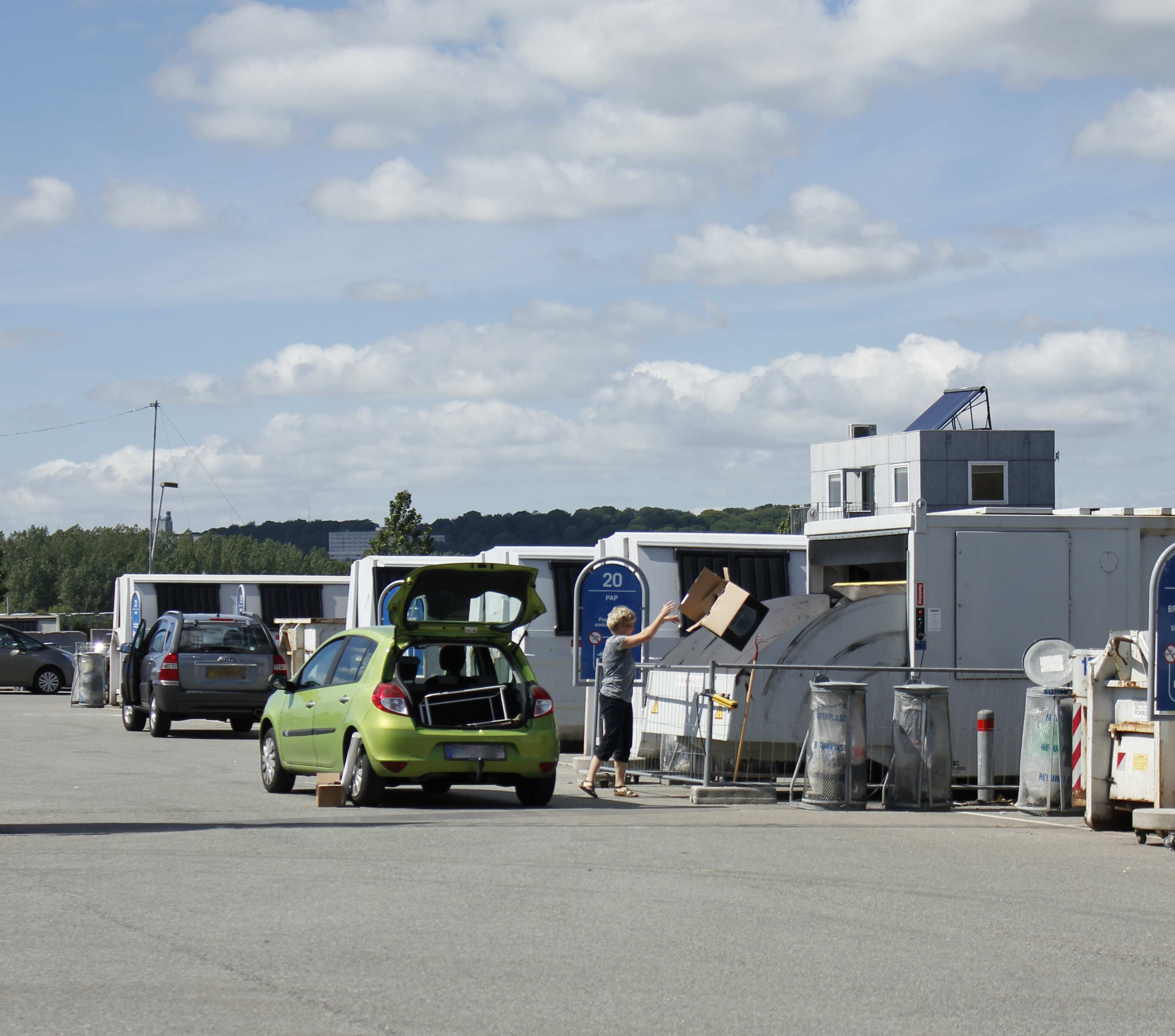 Kvinde smider papkasse i container på genbrugspladsen